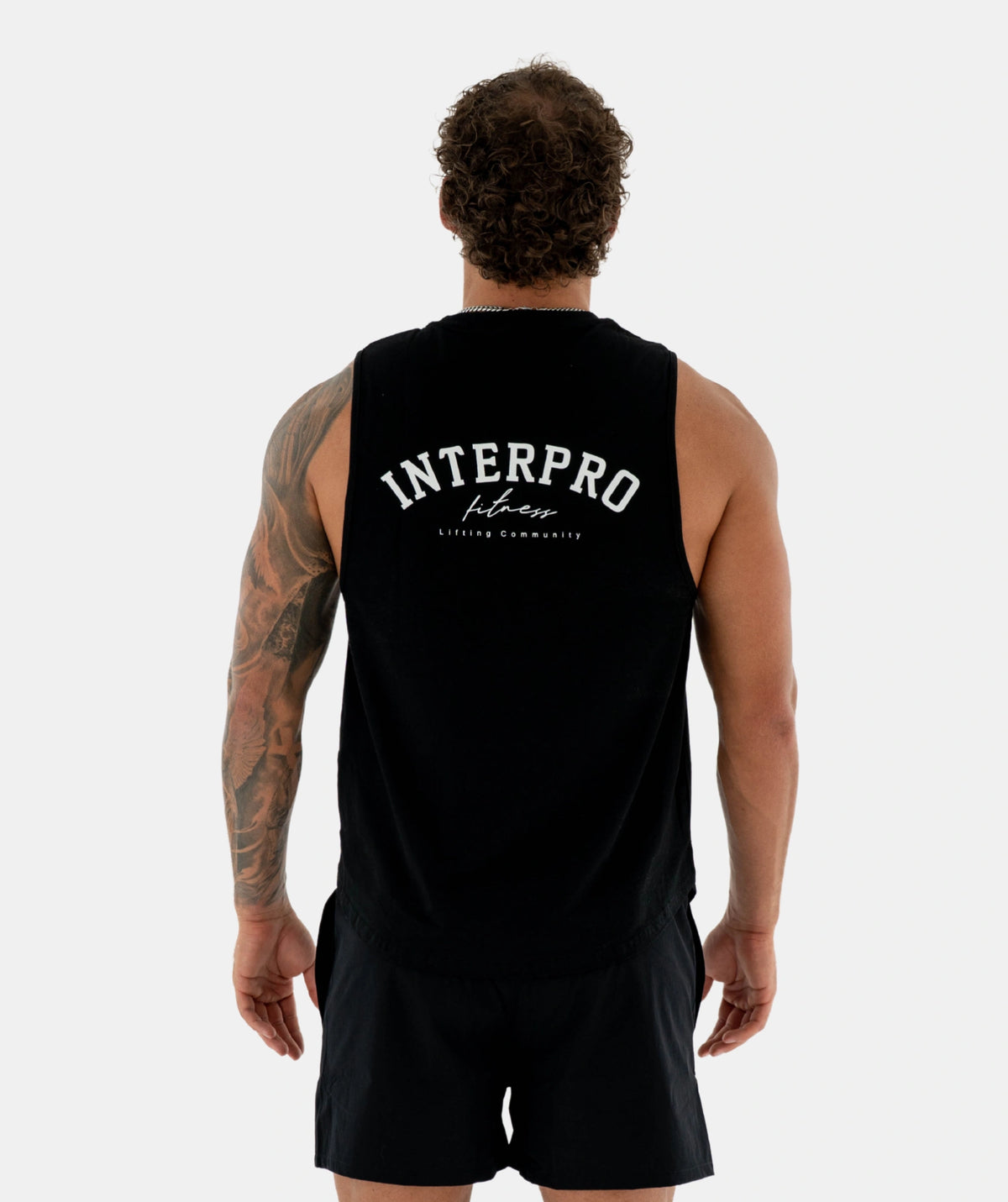 A man viewed from behind wearing a black sleeveless athletic tank top with 'INTERPRO fitness' printed in white across the back, paired with black shorts, against a light gray studio background.